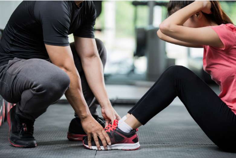 personal trainer holding a woman's feet while she does situps