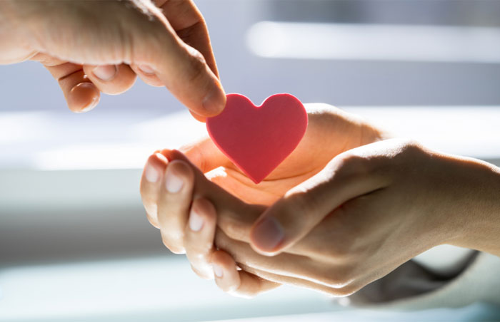ncl close-up photo of one hand putting a red heart into another person's cupped hands