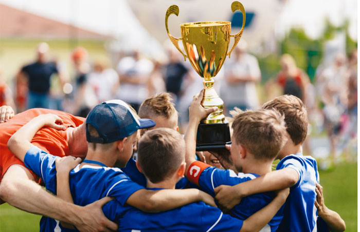team-700px photo of a boys sports team in blue jerseys huddled and holding a trophy overhead