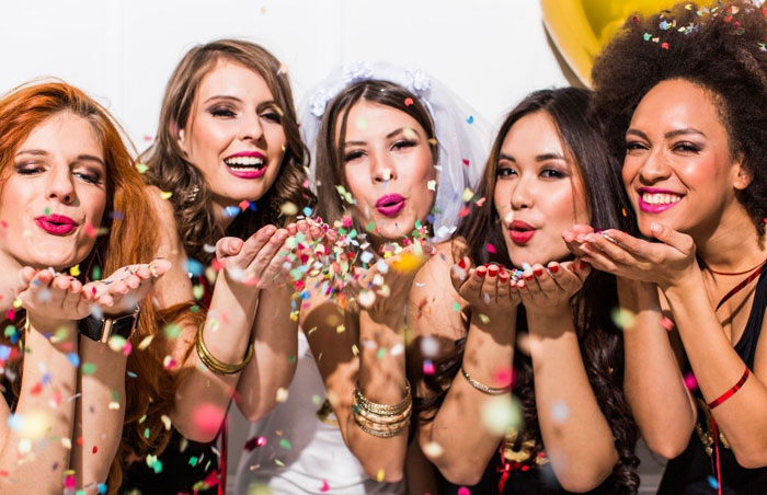 bachelorette photo of five women smiling and blowing confetti from their hands in front of them