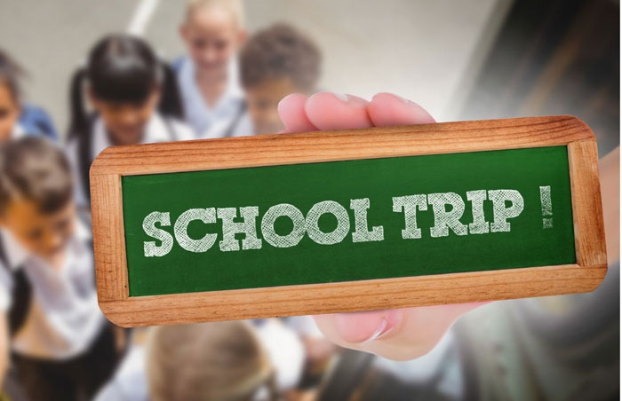 schooltrip photo of a hand holding a small chalkboard that says school trip with the image of children in the background