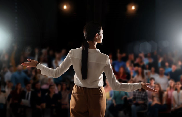 speaker photo of the back of a woman standing in front of an audience with her arms out