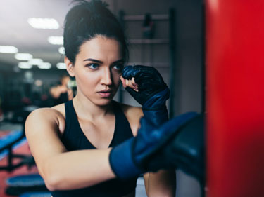 woman wearing boxing gloves punching a bag in cardio kickboxing class