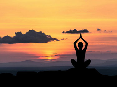 silhouette of a person doing yoga with a sunset behind them