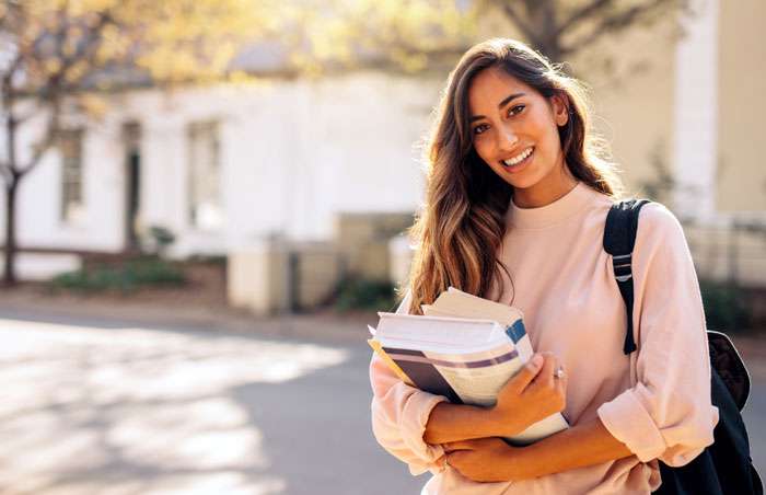 college-student female college student standing outside a building while holding textbooks