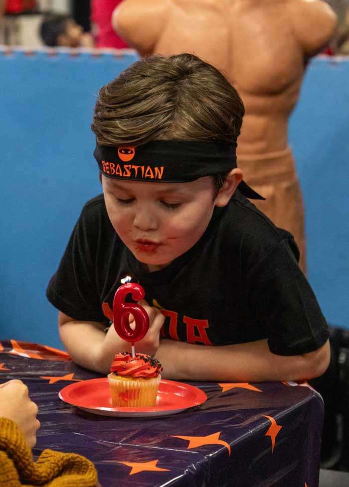 6thbday boy wearing a headband that says sebastian blowing out a candle shaped in the number 6 at a kids birthday party in roseville at THE STUDIO